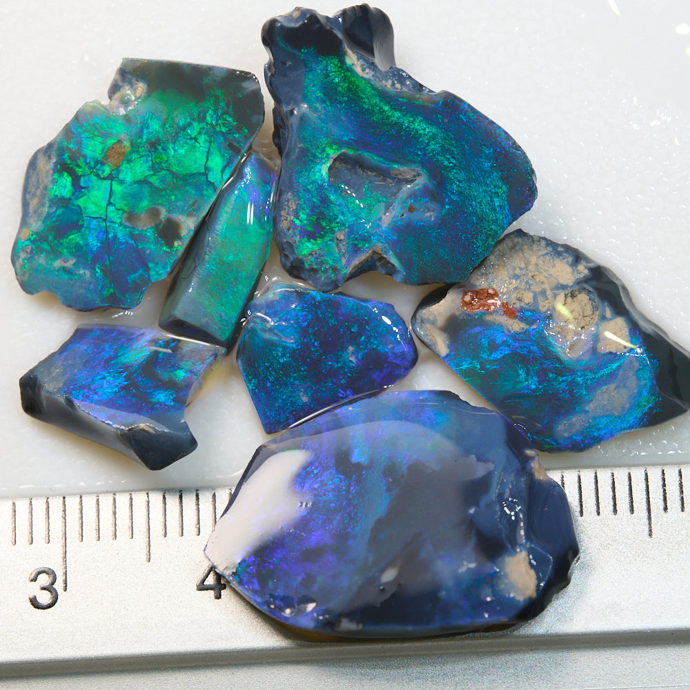 Rough black opal rubs from Lightning Ridge showing green and blue colors, with a scale for size reference.