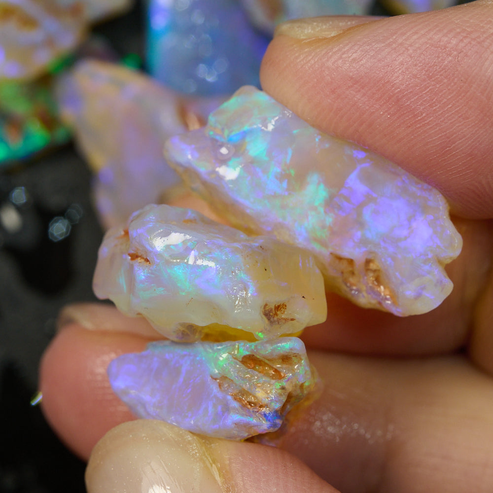 Hand holding rough opal pieces displaying vibrant blue and green colors, ideal for crystal inlay projects.
