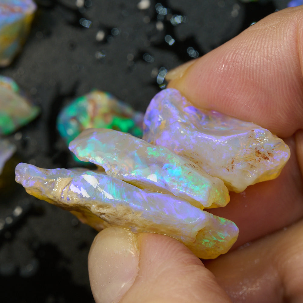 Hand holding multiple rough opal pieces showcasing vibrant green and blue colors against a dark background.