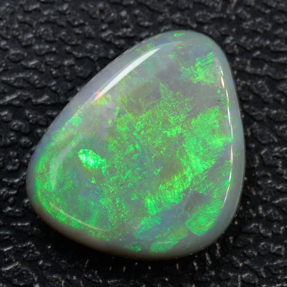 1.46 cts Dark Opal from Lightning Ridge, green triangular solid stone with low dome shape on textured surface.