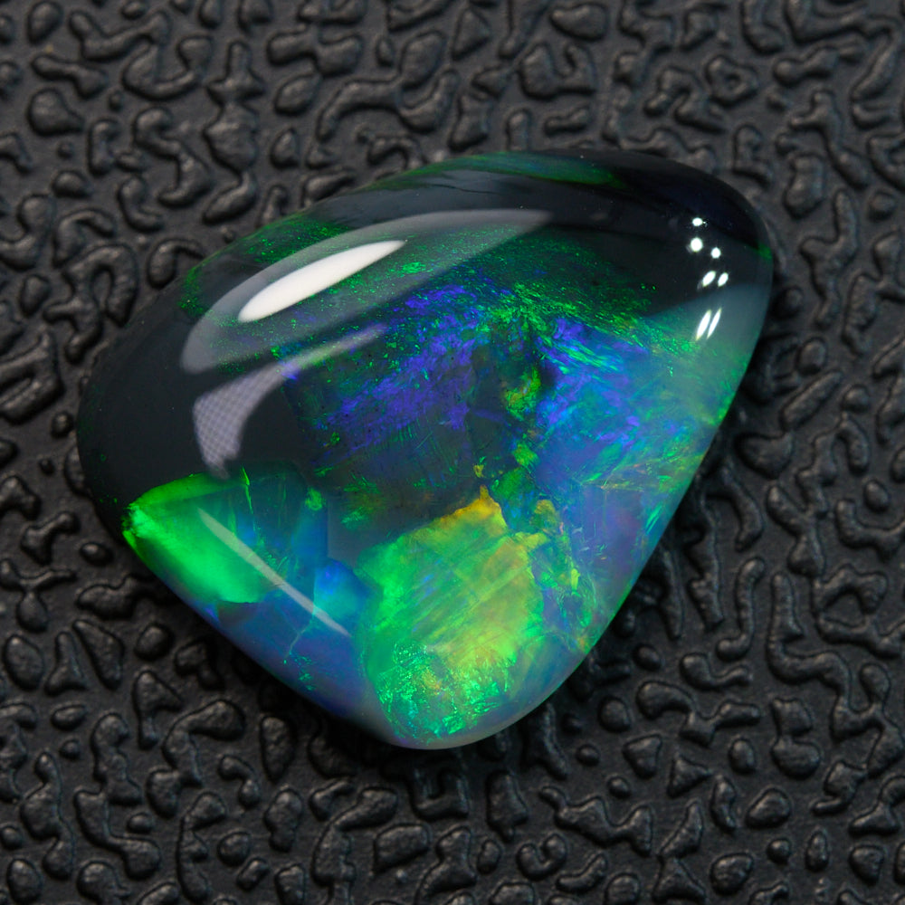 2.90 cts Black Opal from Lightning Ridge showcasing vibrant green and orange hues against a textured black background.