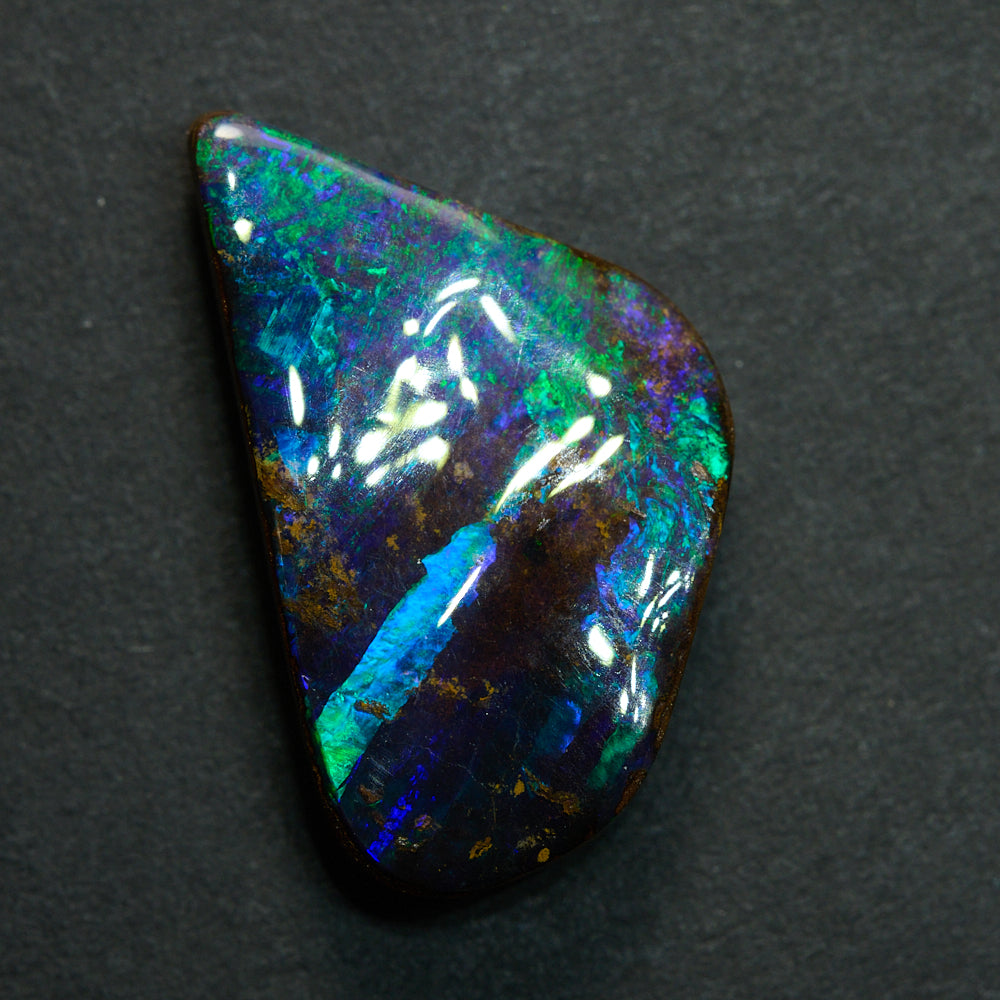Close-up of boulder opal cut stone showing vivid blue green flash and natural ironstone host rock