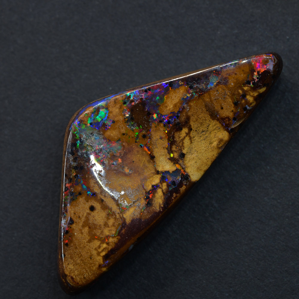A polished boulder opal cut stone displaying vibrant flashes of red and green color within its natural ironstone matrix, with a smooth oval shape and glossy finish